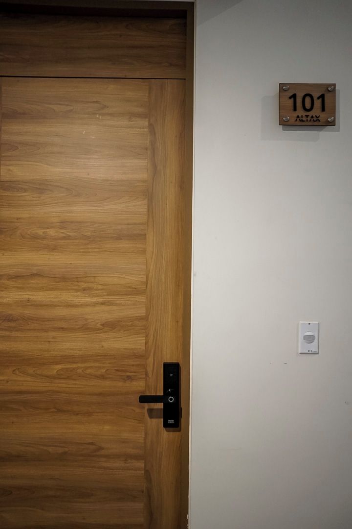A wooden door with a black handle and a wall-mounted sign reading "101 ALTAX".
