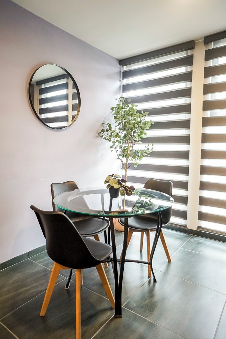 Un área de comedor moderna con una mesa de vidrio, sillas negras y una planta en maceta.