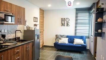 A compact living space with a kitchenette, a blue sofa, and a 'HOME' sign on the wall.