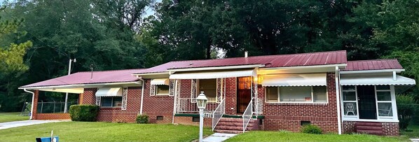 A two-story brick house with a red roof, a porch with white trim, and a 'RENT' sign. - Charming 3-bedroom, spacious home conveniently located near Tuskegee University (Tuskegee)
