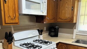 A kitchen with wooden cabinets, a white stove, a microwave, and a coffee maker. - Charming 3-bedroom, spacious home conveniently located near Tuskegee University (Tuskegee)