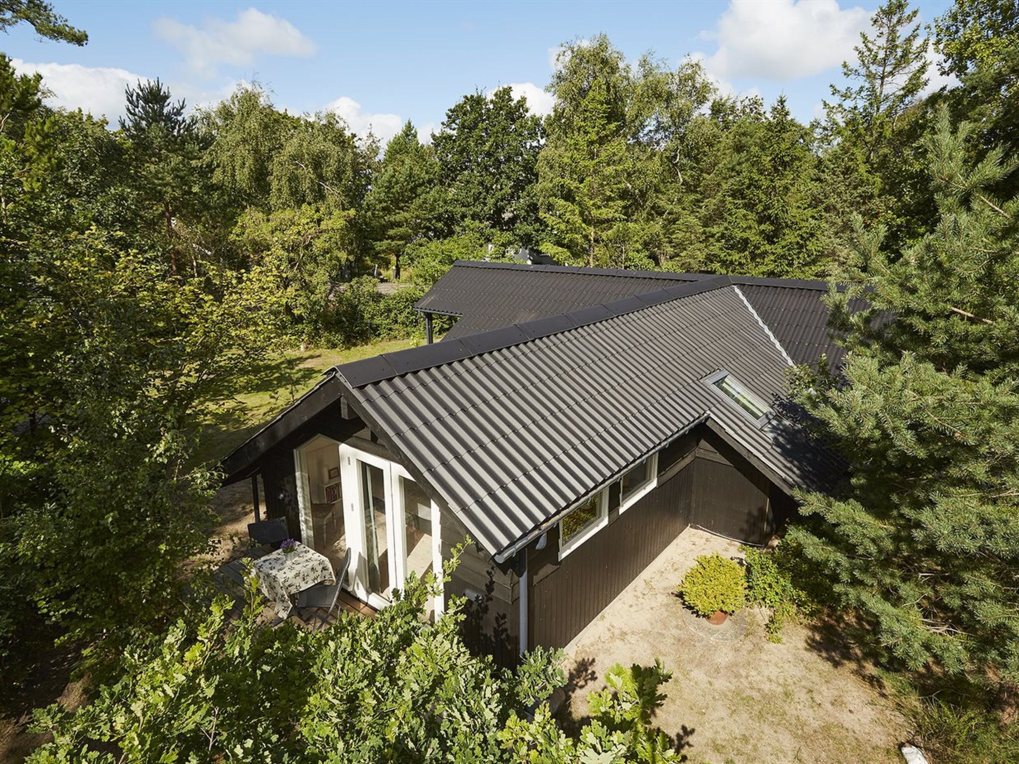 A house with a sloped roof, surrounded by dense forest.