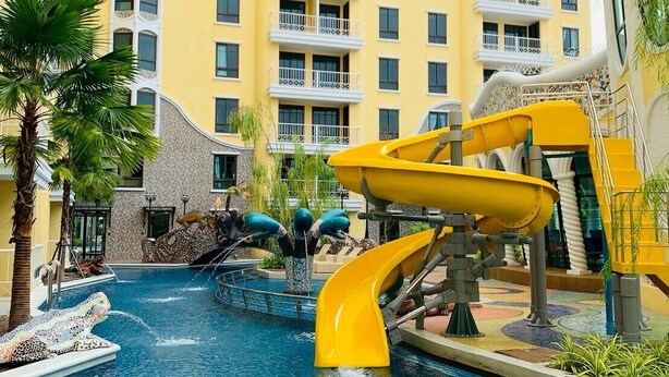 A hotel with a swimming pool, a water slide, and a multi-story building with balconies.