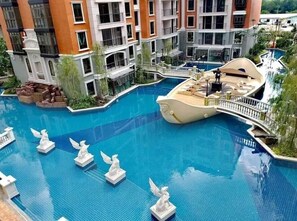 Una piscina con un solárium con forma de barco, rodeada por un edificio de varios pisos con balcones.