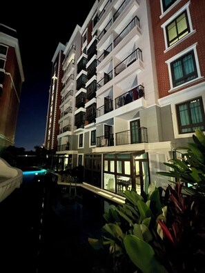 Un hotel de varios pisos con balcones, piscina e iluminación exterior por la noche.