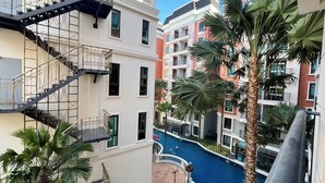 A multi-story hotel with a central courtyard featuring a swimming pool, surrounded by palm trees and other greenery.