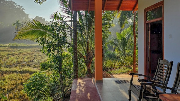 Un porche techado con vistas a un paisaje exuberante, muebles de madera y cielo despejado.