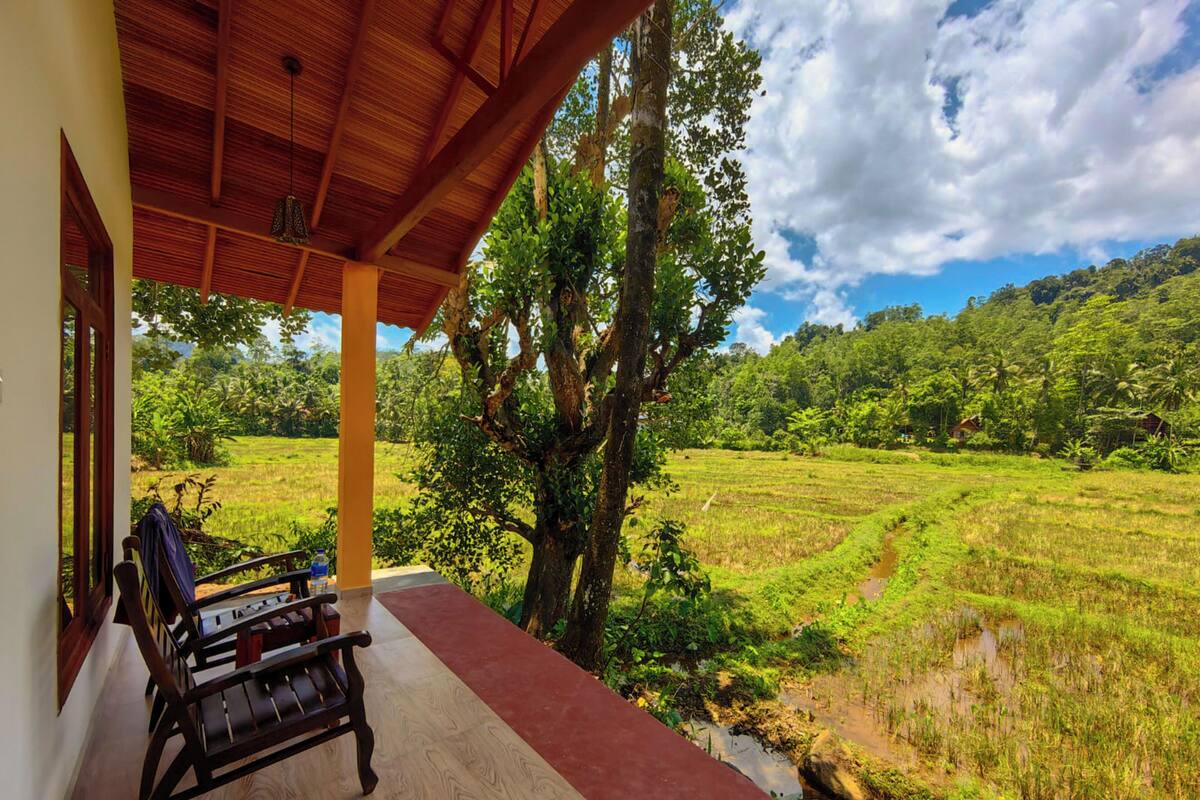 A wooden veranda with a bench, overlooking a lush green landscape with a river and trees.