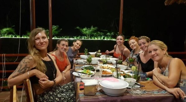 A group of people dining at an outdoor table with a view of greenery and a thatched roof structure. - Forest & Fields Sinharaja  (Deniyaya)