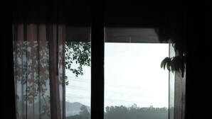 A room with a view of a green field through a window with sheer curtains. - Forest & Fields Sinharaja  (Deniyaya)