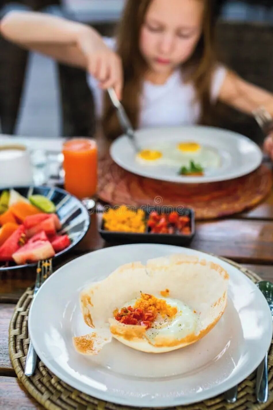 Uma mesa de café da manhã com um prato de ovos, uma tigela de frutas e um copo de suco de laranja.