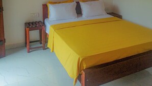 Una cama individual con una colcha amarilla en una habitación con paredes blancas y techo de madera.