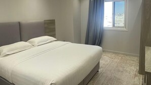 Un dormitorio moderno con una cama grande, iluminación empotrada en el techo y vistas de la ciudad a través de una ventana.