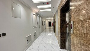 Un pasillo moderno de hotel con piso de mármol, iluminación empotrada y una pared de mármol con un panel de control.