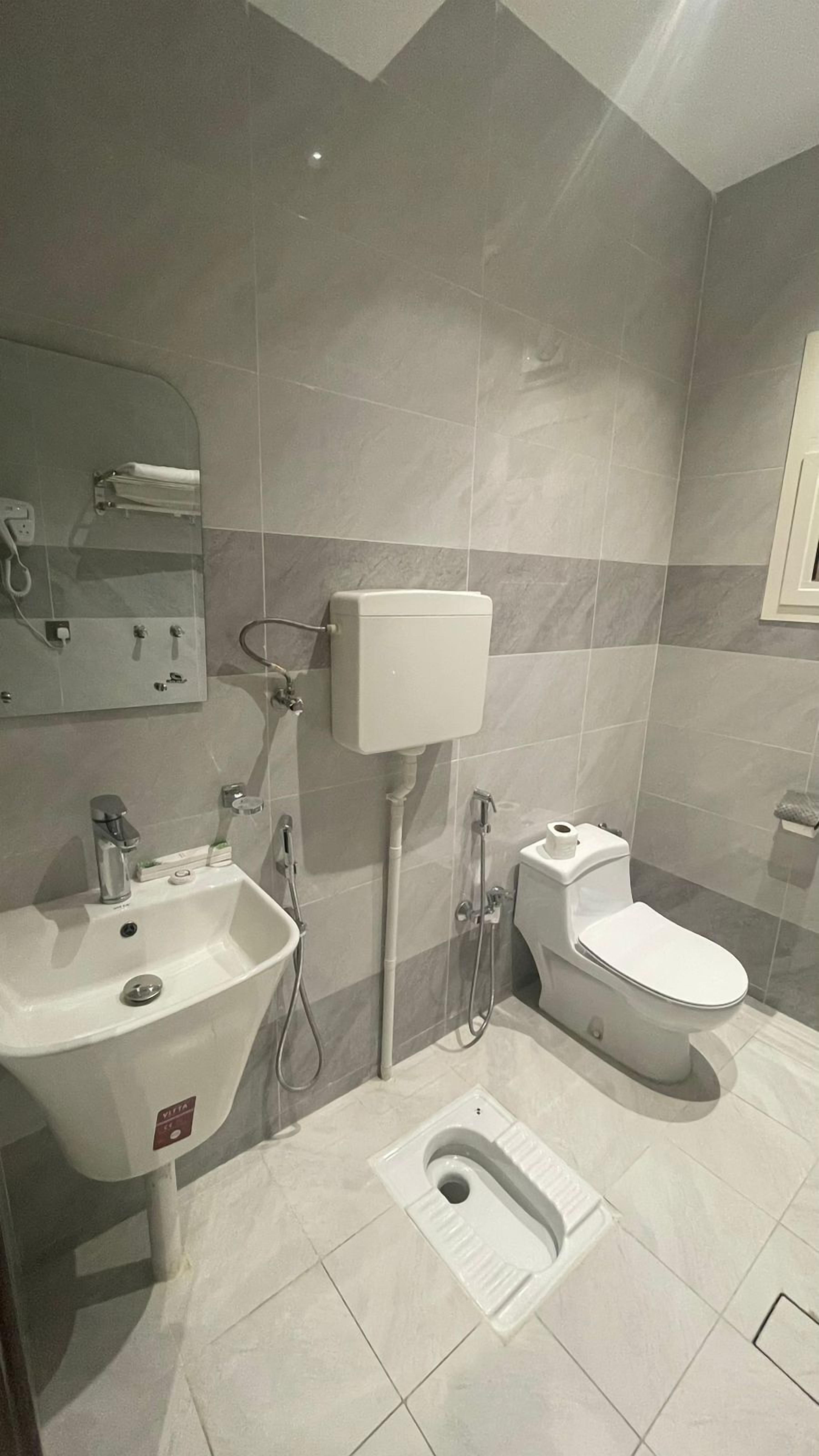A modern bathroom with a sink, toilet, bidet, and bidet hose.