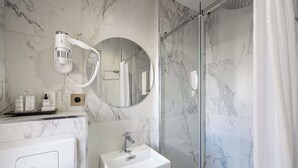 Ein modernes Badezimmer mit Marmor-Spritzschutz, einem runden Spiegel, einem weißen Waschbecken und einer Duschkabine aus Glas.