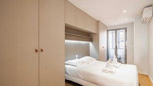 Une chambre d’hôtel moderne, dotée d’un lit, d’une armoire intégrée et donnant sur l’extérieur grâce à une porte vitrée.