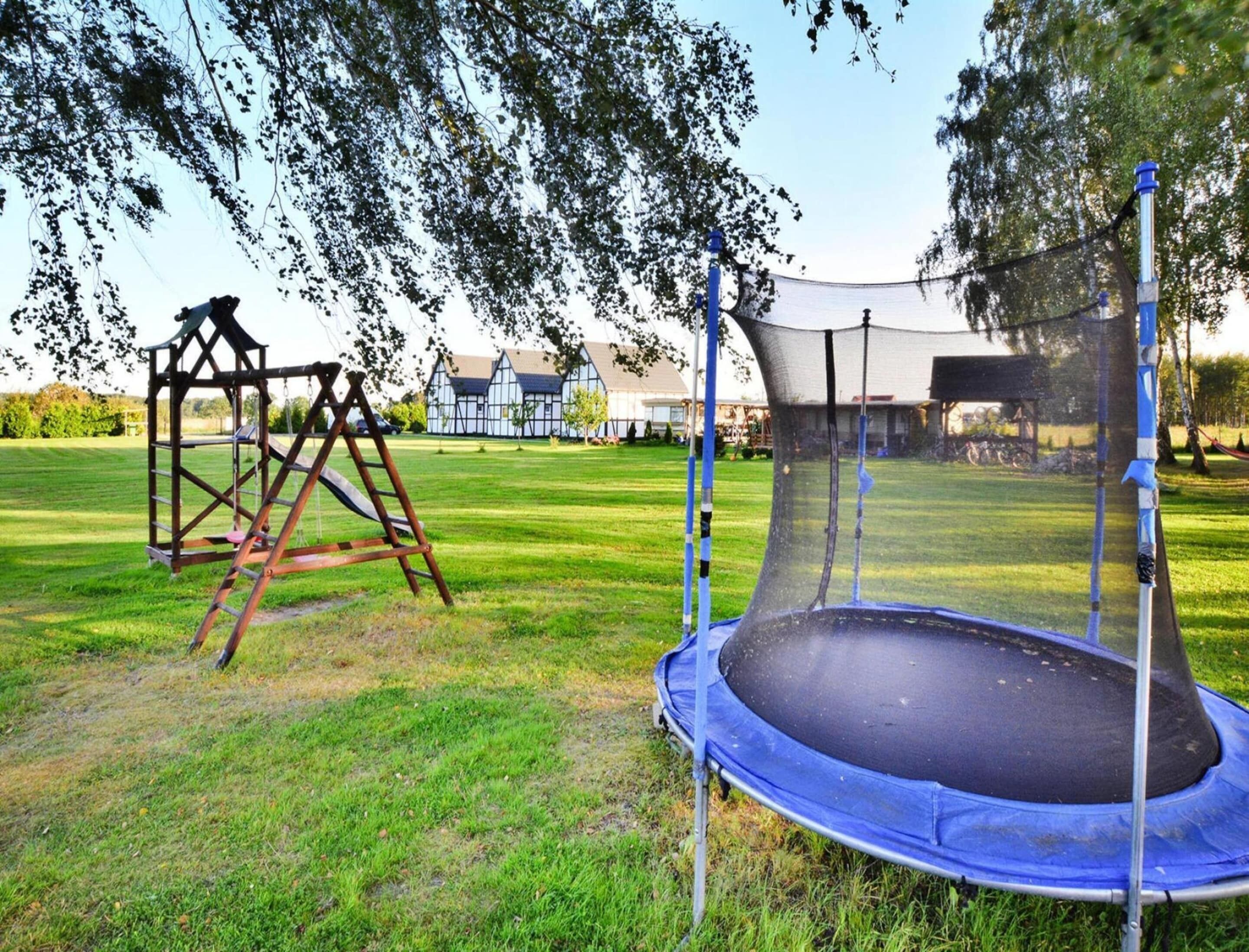 A trampoline in a grassy yard with a swing set and a house in the background.