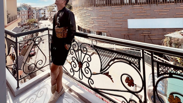 Eine Person steht auf einem Balkon mit Blick auf ein modernes Gebäude, das eine geschwungene Fassade und ein verziertes Metallgeländer hat.