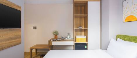 Una camera d'albergo moderna con un letto grande, una scrivania in legno con un computer, un tavolino e uno scaffale con articoli da toilette.