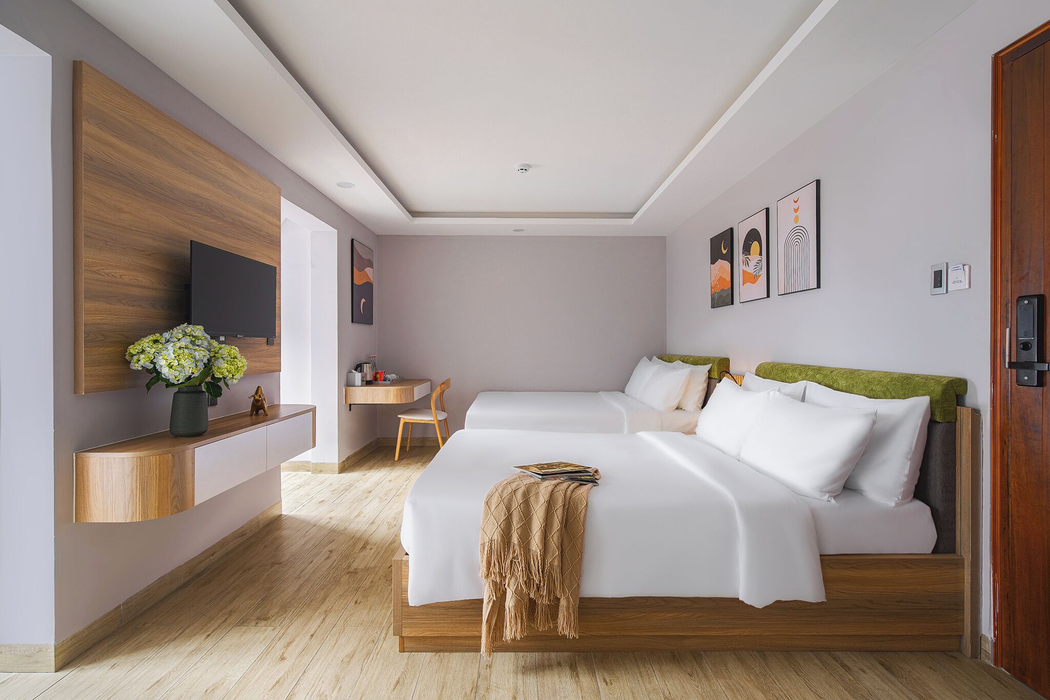 A modern bedroom with a wooden headboard, a bedside table, a TV mounted on the wall, and a desk with a chair.