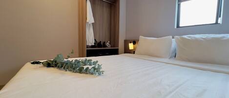 Una cama bien tendida con ropa blanca, una mesita de noche con lámpara y un armario de madera con espejo.