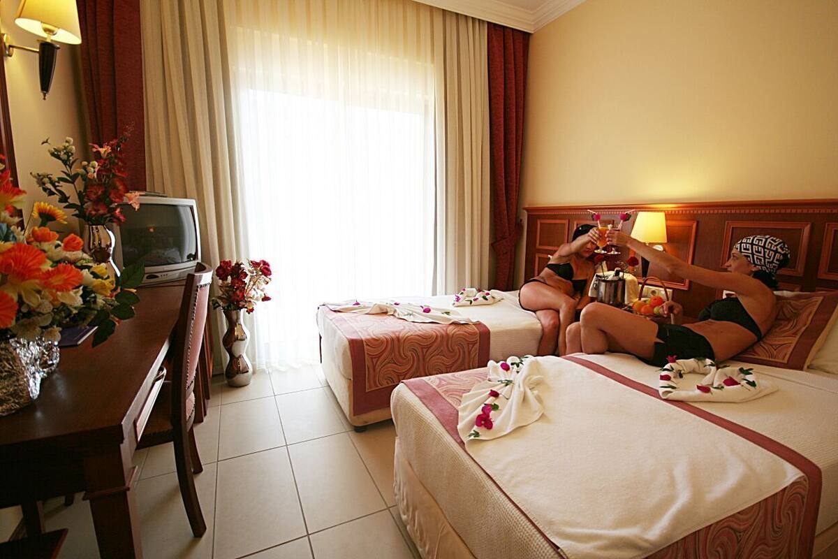 A hotel room with two beds, a desk, a television, and a window with curtains.