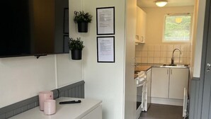 A compact kitchen with white cabinetry, a built-in microwave, and a small window. - Ystad Camping (Ystad)