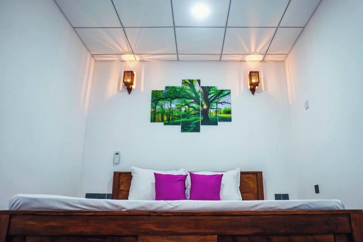 Ein Schlafzimmer mit einem hölzernen Bett, weißer Bettwäsche, zwei Wandleuchten und einer Gruppe von drei gerahmten Landschaftsbildern.