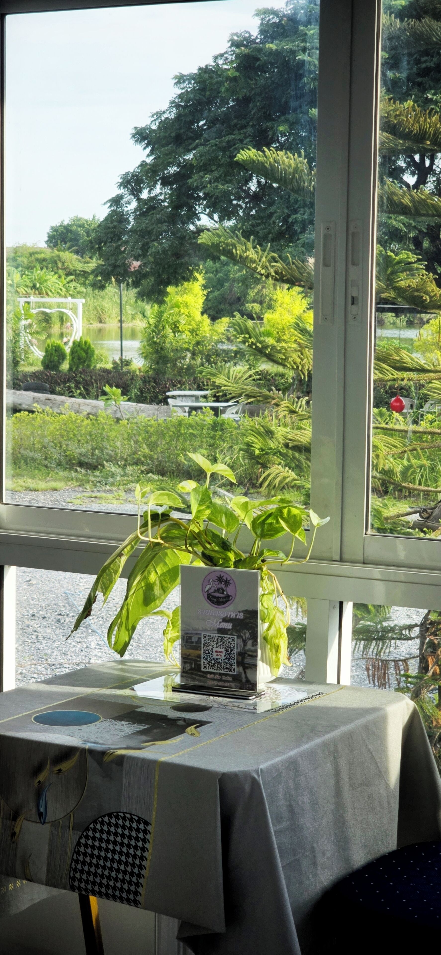 A table with a tablecloth and a potted plant, a window with a view of a garden.