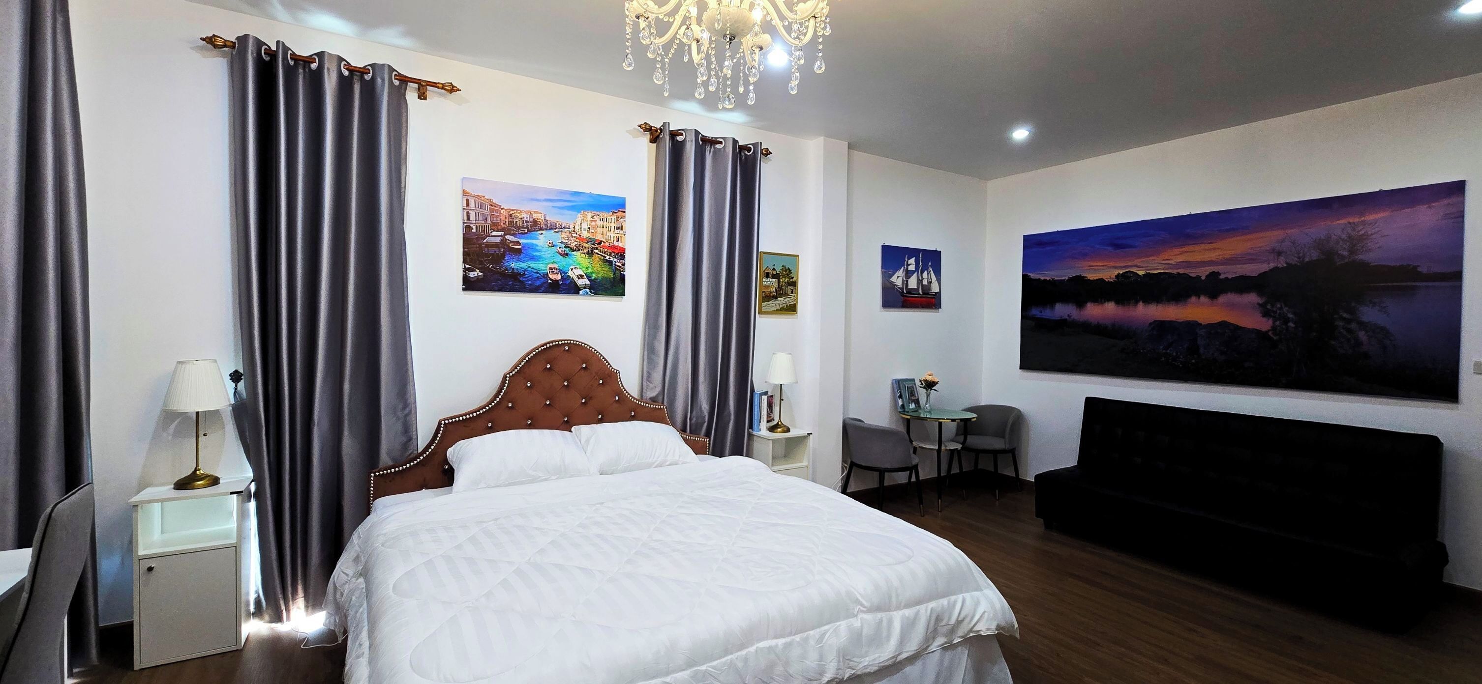 A hotel room with a large bed, a desk, a chair, a small table, and a TV.