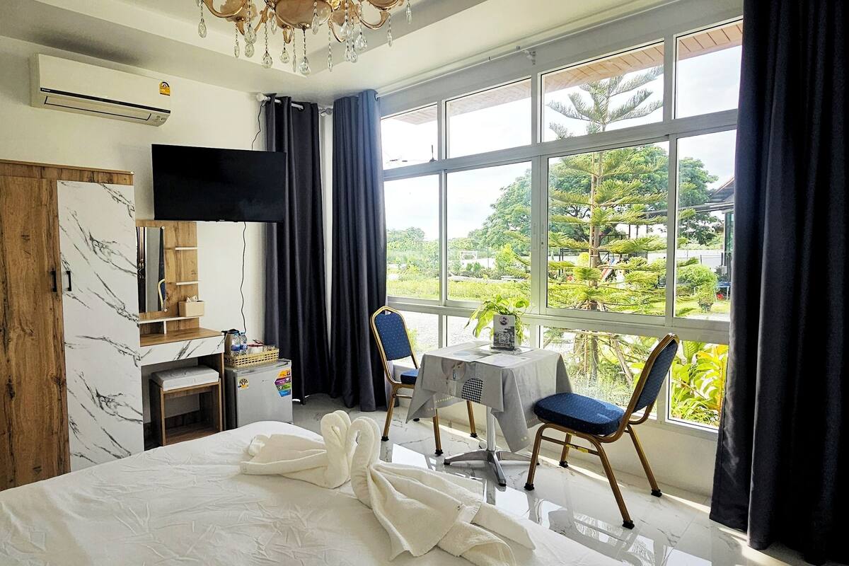 Ein Hotelzimmer mit Bett, Schreibtisch mit Stuhl, Fernseher und Fenster mit Blick auf Grünfläche.