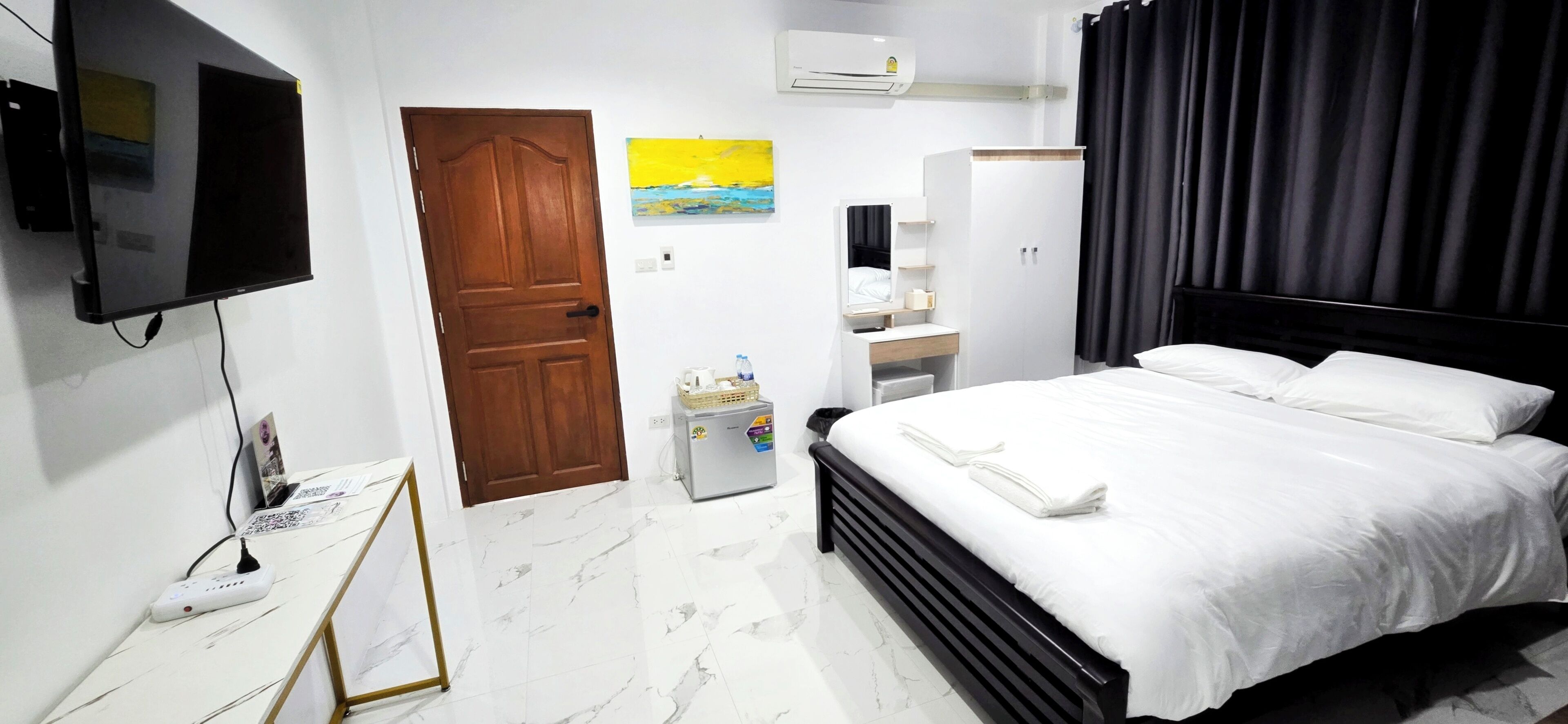 A hotel room with a bed, a TV, a desk with a computer, a wardrobe, and a painting on the wall.
