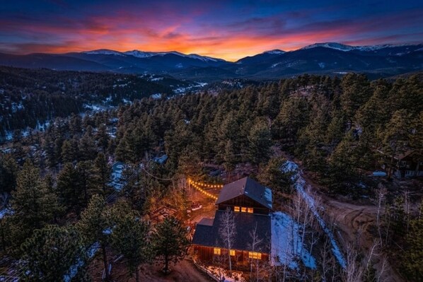 A lodge surrounded by a forest with a mountain range in the background.