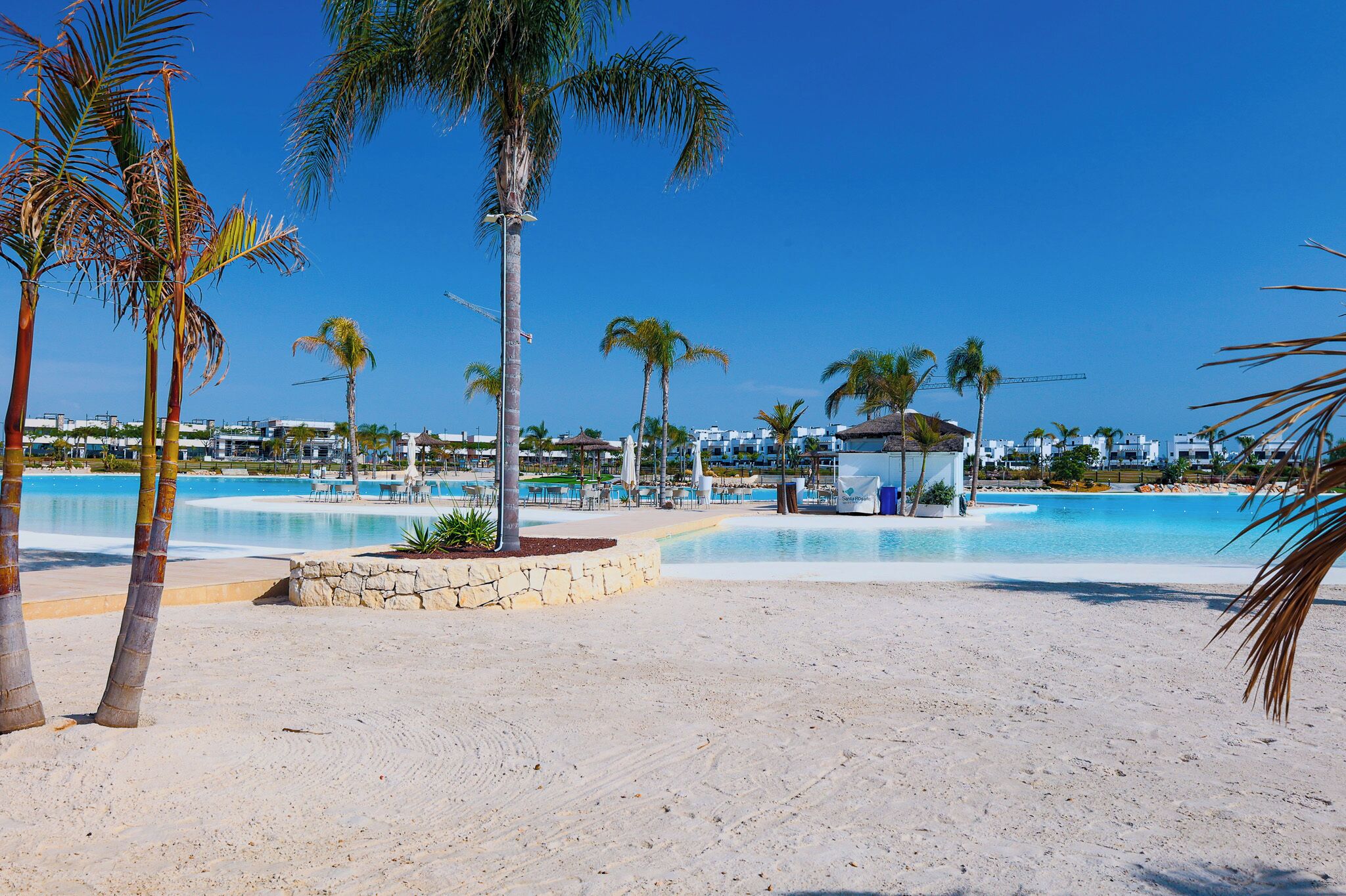 A beach resort with a large pool, palm trees, and a gazebo.