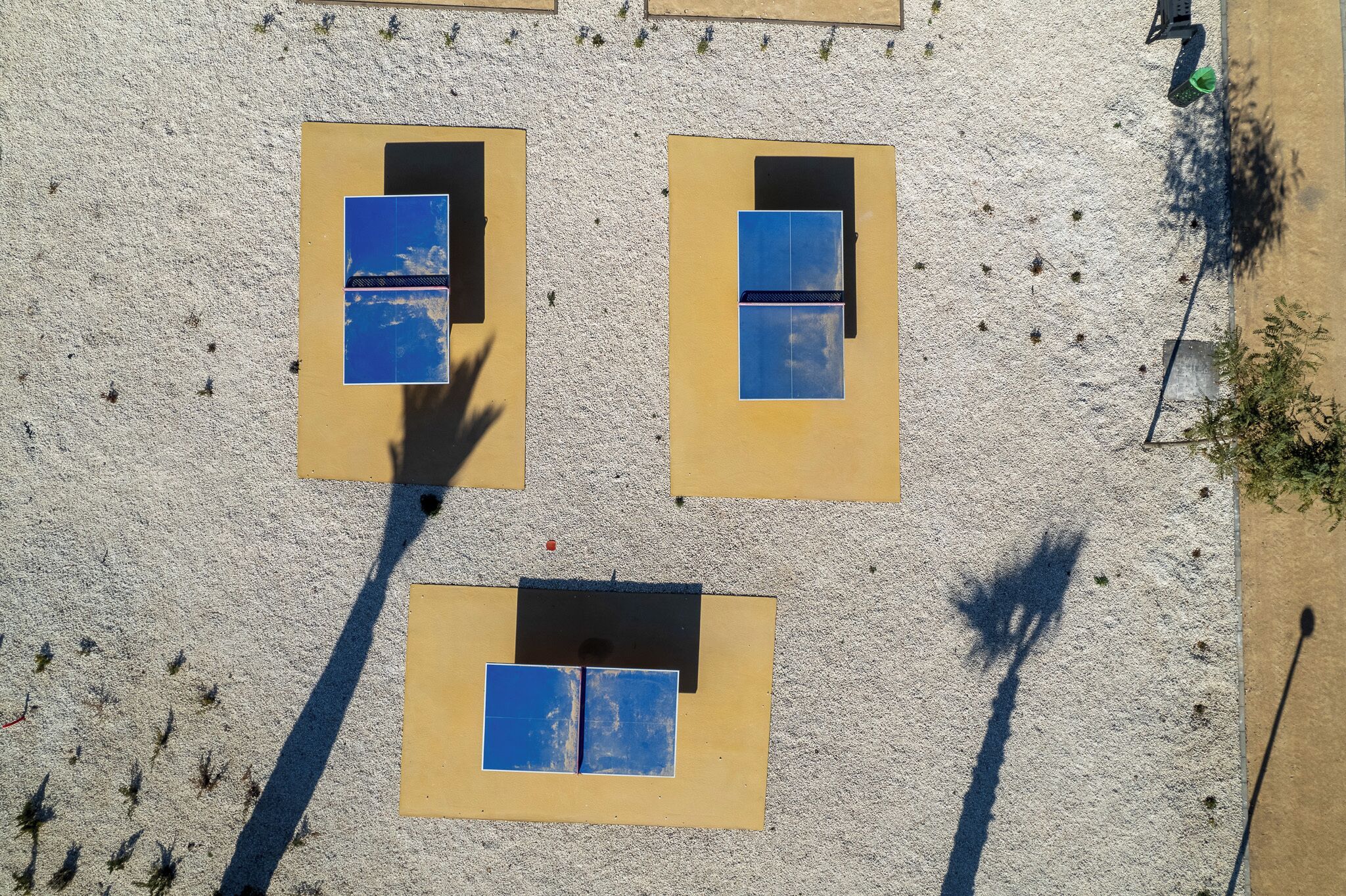 Une vue aérienne d’une plage où l’on aperçoit trois chaises longues alignées, chacune étant dotée d’un tapis bleu et d’une housse noire.