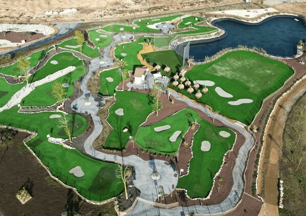 An aerial view of a golf course with multiple greens, sand traps, and a water hazard.