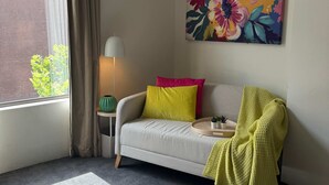 A cozy room with a sofa, a lamp, a painting, and a window with curtains.