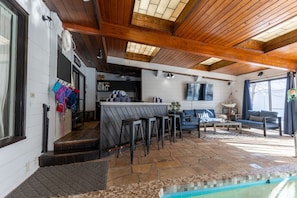 A covered outdoor area with a pool, bar, seating, and a kitchen area.