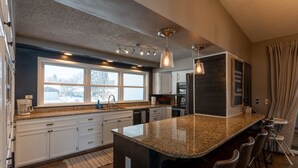 A modern kitchen with granite countertops, white cabinetry, a large island with bar stools, and pendant lighting. - Historic home w/ indoor pool on Iconic 8th St (Fargo)