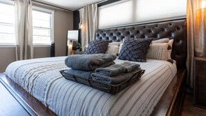 A neatly made bed with a striped bedspread, a dark headboard, and a stack of folded towels. - Historic home w/ indoor pool on Iconic 8th St (Fargo)