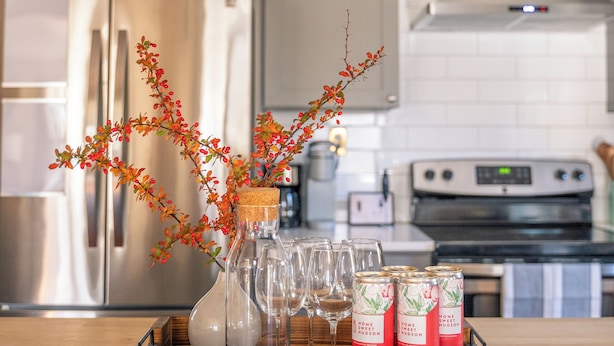 A kitchen with a wooden countertop, a vase with branches, wine glasses, and canned drinks.