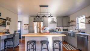 A modern kitchen with a large island, bar stools, stainless steel appliances, and a view of the outdoors.