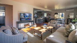 A spacious living area with a television, sofas, a coffee table, and a kitchen in the background.