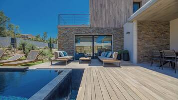 Un espace piscine extérieur moderne, doté d’une terrasse en bois, de chaises longues et d’un mur en pierre.
