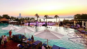 A pool area with lounge chairs and umbrellas, a sunset view, and a distant city skyline. - Palm Jumeirah, Studio, Fantastic sea, beach and skyline view, Beach  (Dubai)