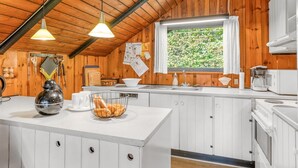 Una cocina con paredes de madera, armarios blancos, un ventanal grande y una lámpara colgante.