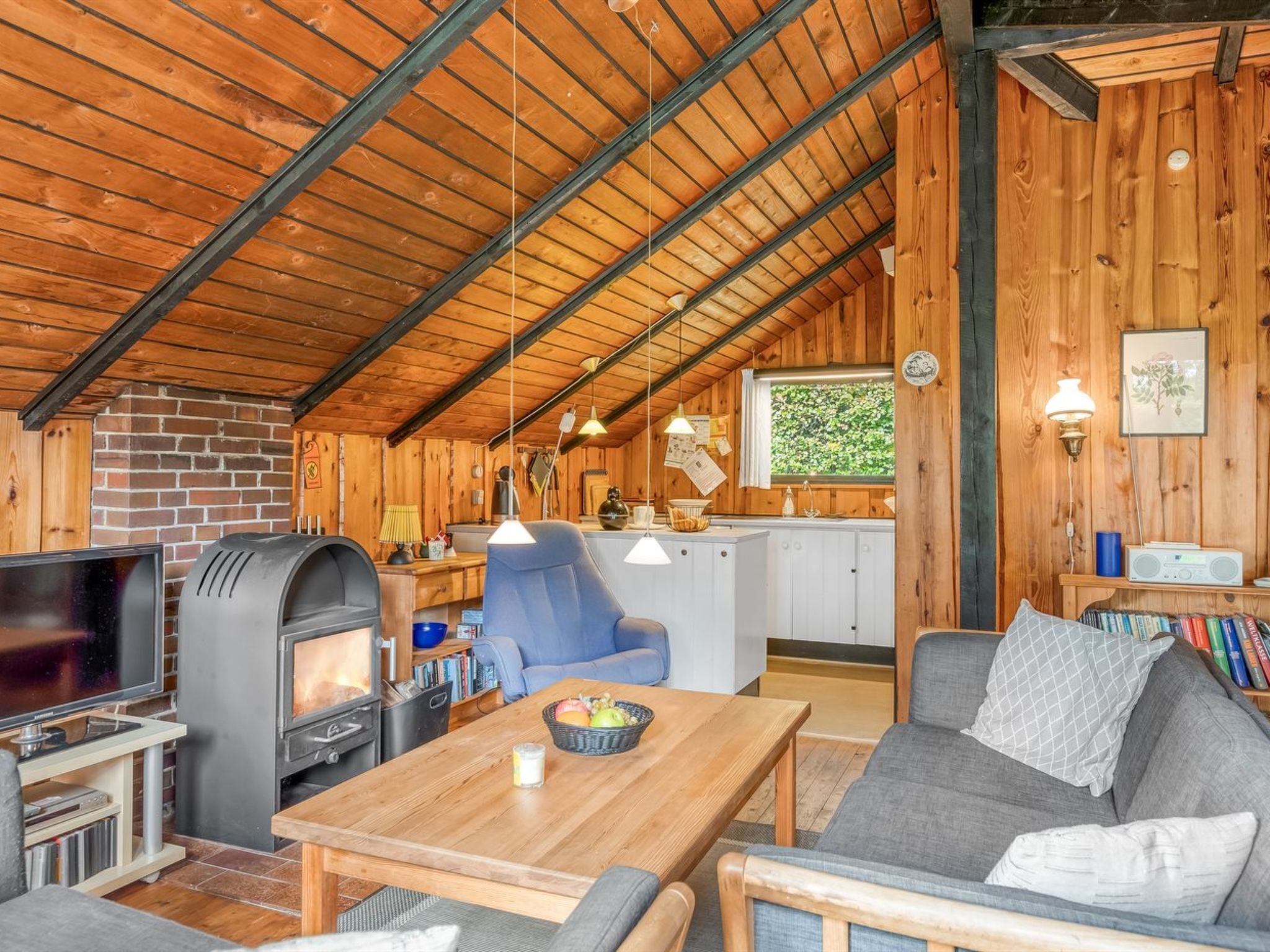 Een gezellig chaletinterieur met houten plafond, open haard, televisie, eethoek en keuken.