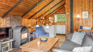 Interior acogedor de una cabaña con techo de madera, chimenea, televisor, comedor y cocina.