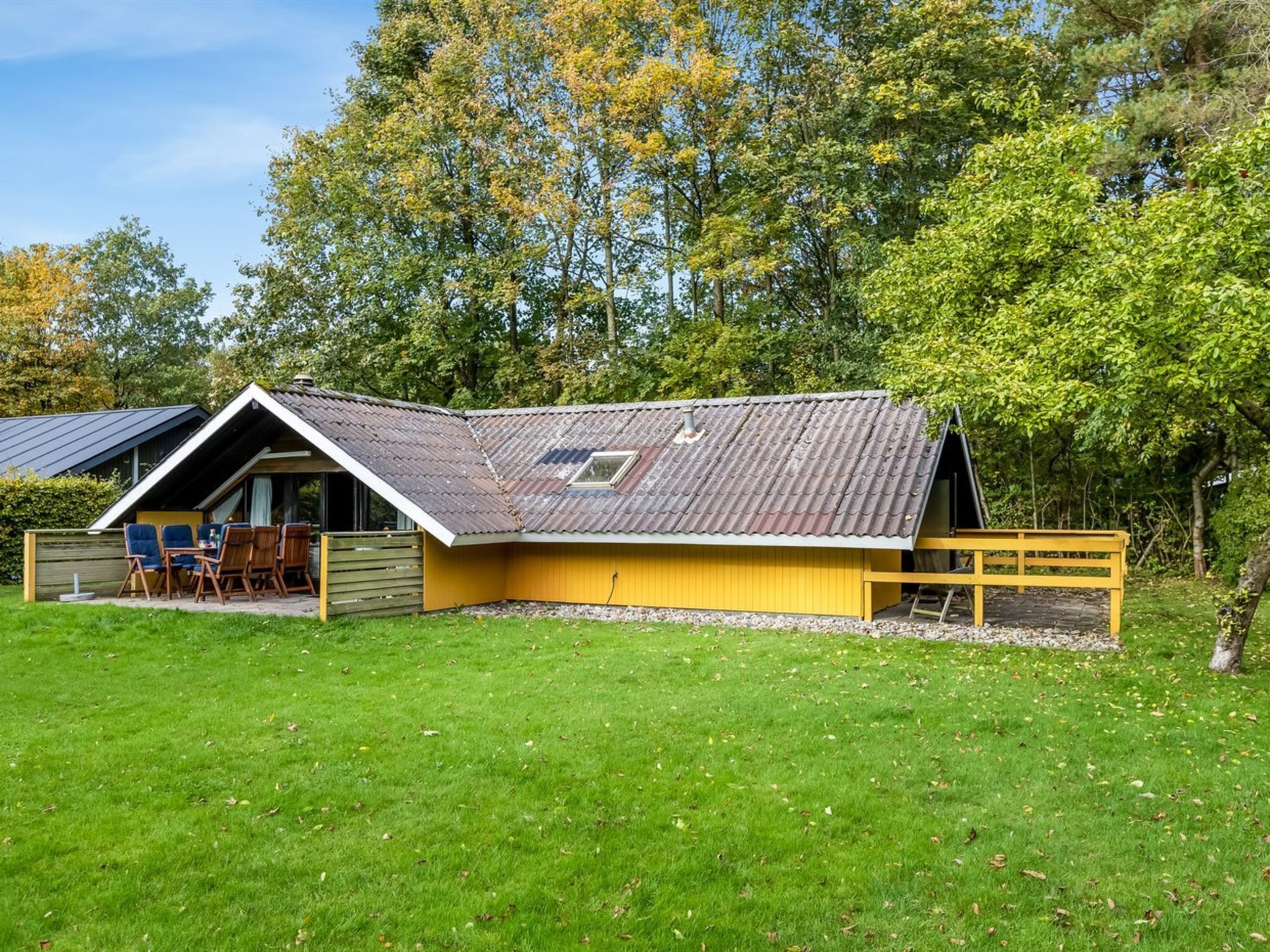 A yellow building with a sloped roof, a fenced patio area, and a small table and chairs outside.